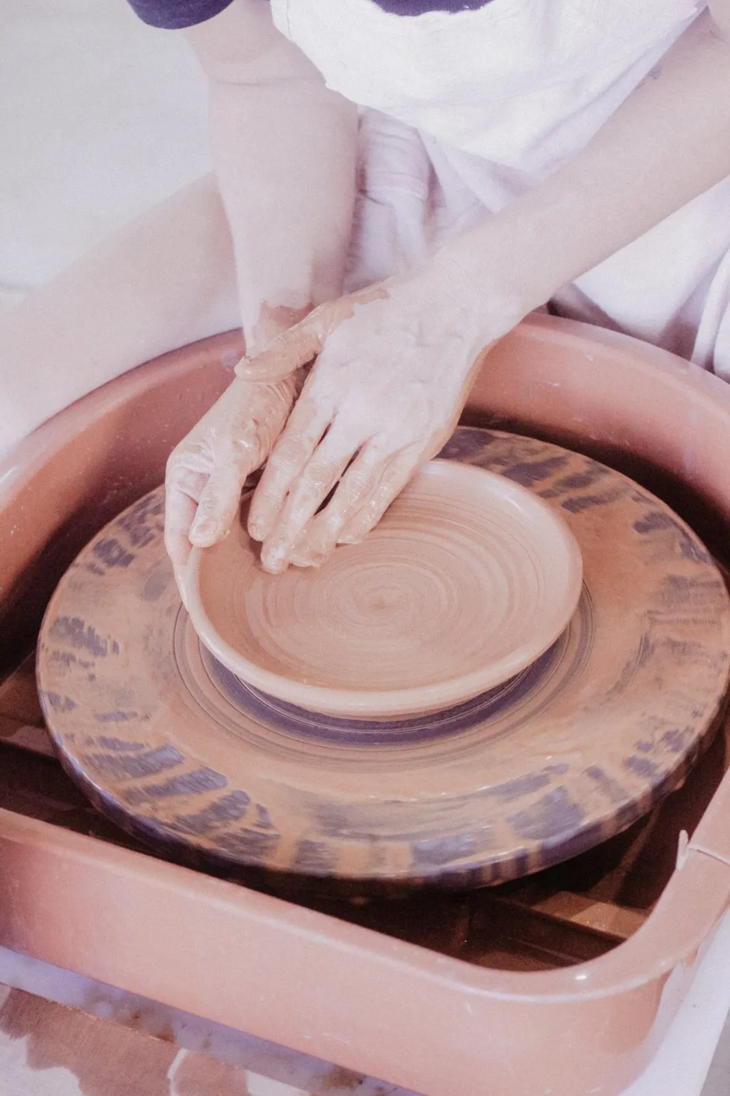 Hands shaping clay on the wheel at Studio Mano